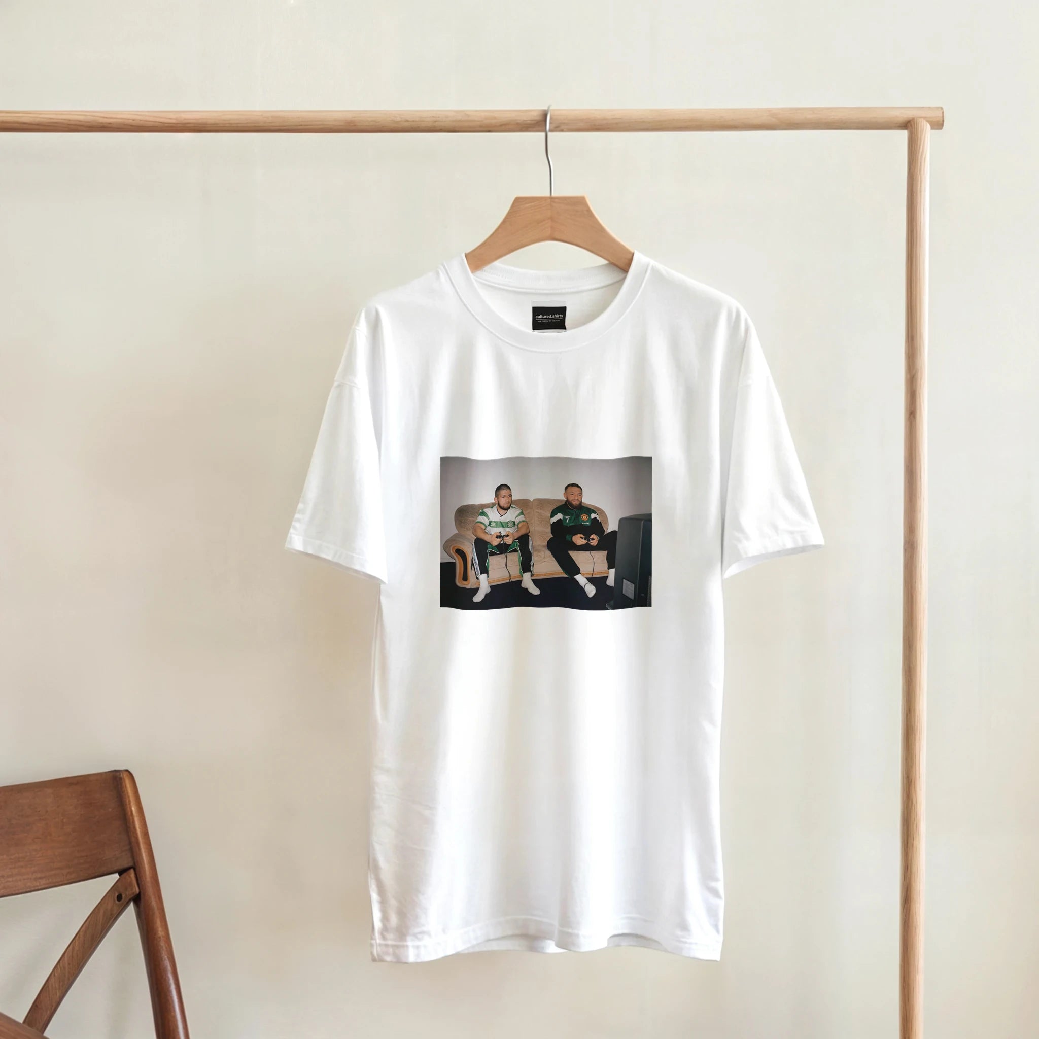 White T-shirt hanging on a wooden hanger, rectangular front graphic with two men.