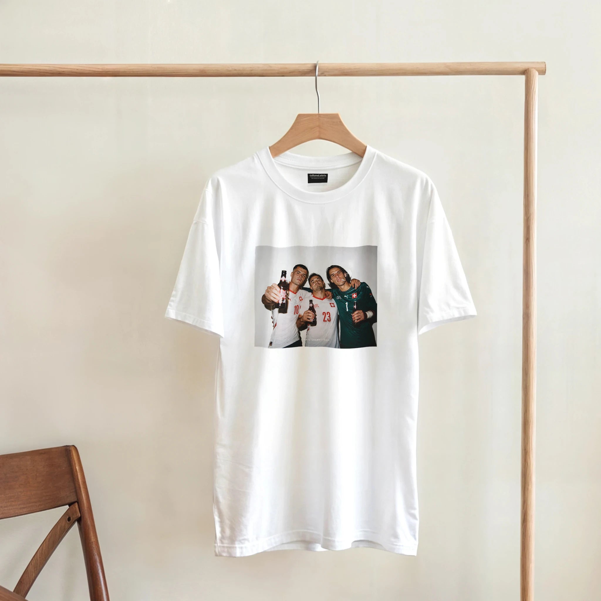 White T-shirt hanging on a wooden hanger, featuring a centered rectangular player graphic